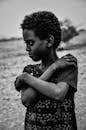 Black and white portrait of an African child with curled hair, looking contemplative outdoors.