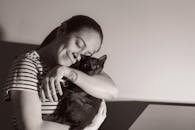 A woman lovingly hugs her black cat indoors, expressing warmth and affection.